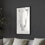 Vue large d'un salon moderne avec canapé gris clair, décoré par un tableau de cheval blanc encadré en noir.