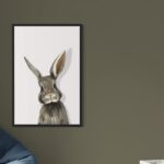 Tableau de lapin avec cadre noir en caisse américaine, accroché dans une chambre d'enfant à côté d'un pouf bleu.