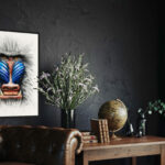 Tableau vertical grand format d'un Mandrill aux couleurs vives, accroché sur un mur noir texturé au-dessus d'un canapé en cuir marron type Chesterfield.