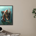 Tableau vertical grand format représentant un poulpe rouge et or dans l'eau bleue, accroché sur un mur beige à côté d'une plante verte.